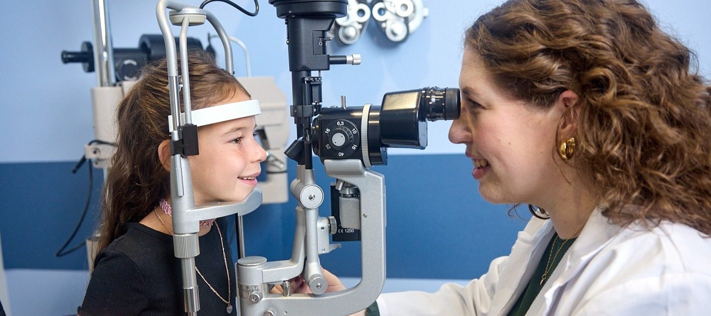 Female presenting eye doctor inspecting female presenting child's eyes