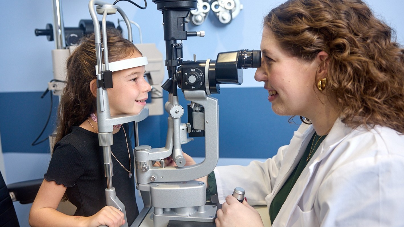 Female presenting eye doctor inspecting female presenting child's eyes