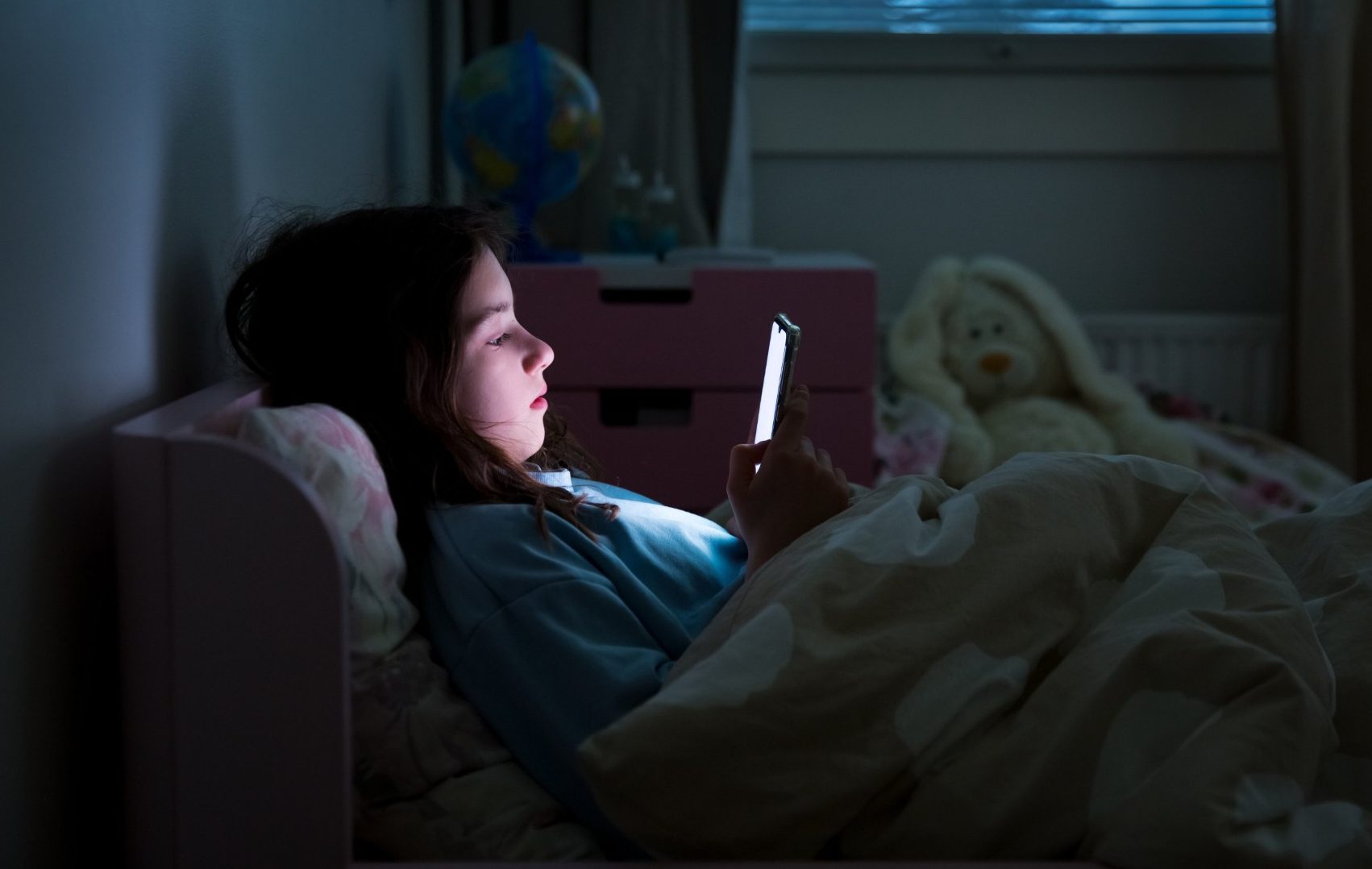 Child in bed in dark looking at bright screen of phone