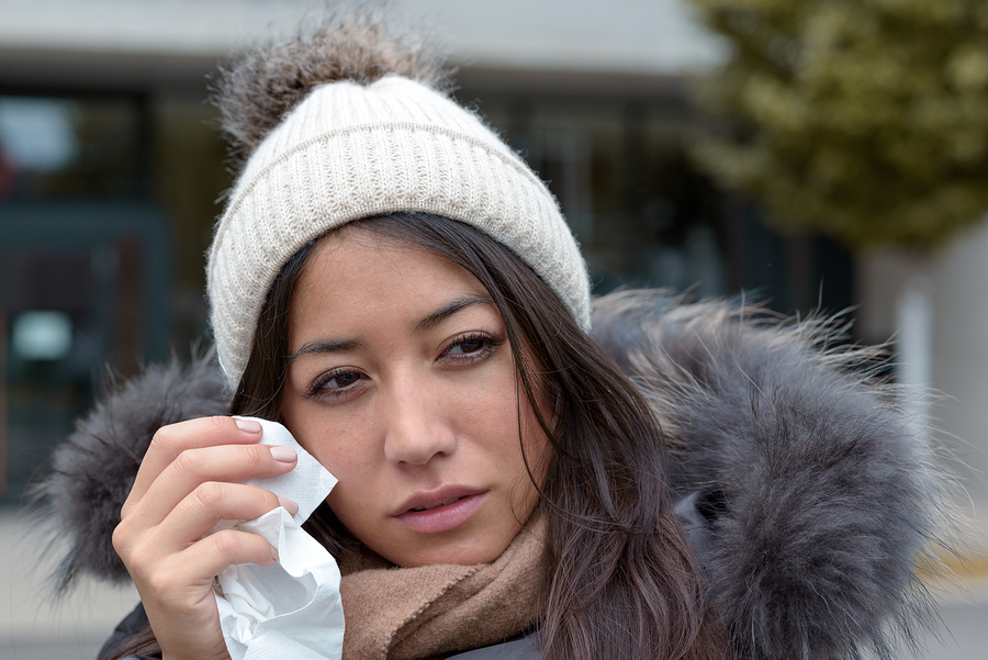 Sad tearful woman in warm winter fashion holding a handkerchief to her face to dry the tears from her eyes looking to the right of the frame with lack lustre eyes and woebegone expression