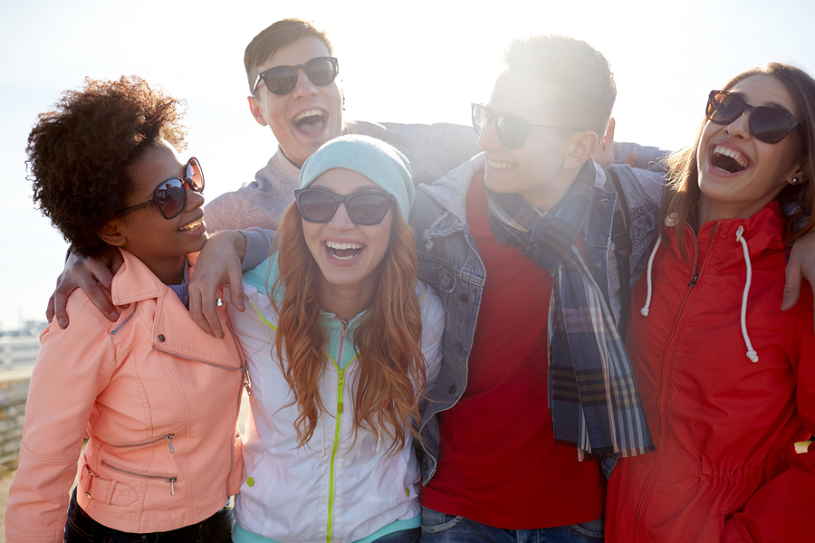 tourism, travel, people, leisure and teenage concept - group of happy friends in sunglasses hugging and laughing on city street